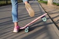 Close-up legs of girl skateboarder in blue jeans and pink sneakers, riding pink penny skate longboard.