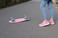 Close-up legs of girl skateboarder in blue jeans and pink sneakers, riding pink penny skate longboard.