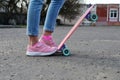 Close-up legs of girl skateboarder in blue jeans and pink sneakers, riding pink penny skate longboard.