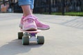 Close-up legs of girl skateboarder in blue jeans and pink sneakers, riding pink penny skate longboard.