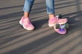 Close-up legs of girl skateboarder in blue jeans and pink sneakers, riding pink penny skate longboard.