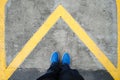 Close up on the legs of a man standing on a yellow triangle in the shape of an arrow, man standing on an arrow in a forward direct