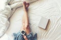 Close up legs women on white bed. Women reading book and drinking coffee in morning relax mood in winter season Royalty Free Stock Photo