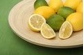 Close-up of lemons and limes on a wooden plate on green background