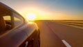 CLOSE UP: Sunrise illuminates the black sportscar cruising along a freeway. Royalty Free Stock Photo