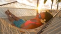 LENS FLARE: Golden sunbeams shine on relaxed woman swinging in the hammock.