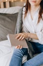 Young girl dressed in beige top sitting on bed with legs crossed, holding open notebook on knees, writing her ideas, future plans Royalty Free Stock Photo