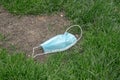 Close up of a light blue doctors face mask or covering with elastic bands laying discarded and littering a parkway in a patch of