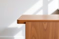 Wooden furniture corner detail with sleek design and light wood grain against a white wall backdrop Royalty Free Stock Photo