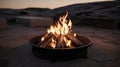 A close-up of a lit campfire in a metal fire pit, with a stone background at dusk Royalty Free Stock Photo