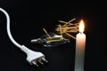 Close-up on a lit candle along with a power cord, light bulb and matches on a black background