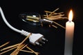 Close-up on a lit candle along with a power cord, light bulb and matches on a black background