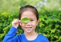 Close up little Asian child girl holding a green leaf closing right eye in green garden background Royalty Free Stock Photo