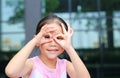 Close up little Asian kid girl with hands glasses in front of her eyes