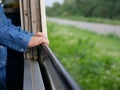 Close up of little baby`s hands holding on a frame of an opened window on a traveling train