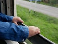 Close up of little baby`s hands holding on a frame of an opened window on a traveling train