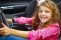 Close up of little beatiful smiling girl sitting in the car pretending to drive the luxury black car, weaing a pink