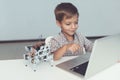 Close up. A little boy is sitting at a table and working behind a gray laptop. Nearby is a small robot Royalty Free Stock Photo