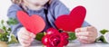 Close up little child girl with flowers holding two red hearts. Wedding, Valentine, love concept
