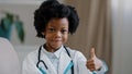 Close-up little cute kid girl in medical gown looking at camera posing indoors smiling pretending be doctor plays nurse