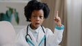Close-up little cute pretty kid girl in medical clothes pretending to be doctor plays looking at camera posing raises Royalty Free Stock Photo