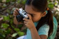 Little girl with backpack taking photo with camera on a sunny day in the forest Royalty Free Stock Photo