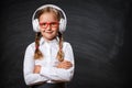 Close-up of a little girl cute student in headphones and glasses on the background of a school black board. Royalty Free Stock Photo