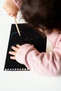 Close up of the hands of a little child drawing on magic scratch painting paper with drawing stick. Royalty Free Stock Photo