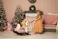 Close up. A little girl pulls a toy rocking horse with a bear in the saddle by the leash. Festively decorated room with a Royalty Free Stock Photo