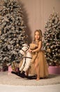 Close up. A little girl riding a toy rocking horse with a teddy bear. Festively decorated room with a Christmas tree Royalty Free Stock Photo