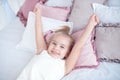 Close-up little girl waking up with stretching arms while awake lying on white bed linen