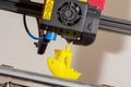 Close-up of little plastic ABS ship model. Yellow filament. Modern 3D printer printerhead with hotend and fan. Royalty Free Stock Photo