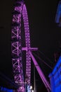 A close up of the London Eye at night lit by purple lights.