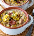 Close up look into a soup crock filled with chicken and corn chowder, topped with grilled corn, bacon and chives.