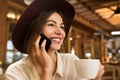 Close up of a lovely girl in hat sitting at the cafe table indoors, holding cup of tea, Royalty Free Stock Photo