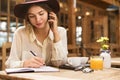 Close up of a lovely girl in hat sitting at the cafe table indoors, talking on mobile phone, Royalty Free Stock Photo