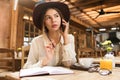 Close up of a lovely girl in hat sitting at the cafe table indoors, talking on mobile phone Royalty Free Stock Photo