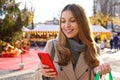 Close-up of lovely smiling young woman using smartphone carrying shopping bags on the Christmas Eve Royalty Free Stock Photo