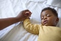 Close Up Of Loving Mother Holding Baby Daughter's Hand As She Sleeps On Bed At Home Royalty Free Stock Photo