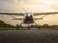 Close-up, low-angle shot of a single-engine propeller plane on a runway with vibrant orange and cloudy sky at dusk. Royalty Free Stock Photo
