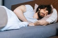 Close-up low-angle view of bearded young man sleeping peacefully lying on side in large comfortable bed under white Royalty Free Stock Photo