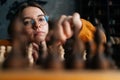 Close-up low-angle view of young woman in elegant eyeglasses making chess move with knight piece sitting in floor Royalty Free Stock Photo
