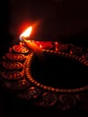 Close up low key indian dipavali oil clay lamp, chirag or panti, shot from side top down angle on a dark black background