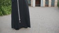 Close-up of the lower body of church minister. Franciscan priest in black long cassock tied with white rope in the