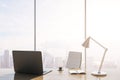 Close up of luxury backlit workplace with laptop, table lamp, coffee cup and panoramic window with city view in the background. 3D