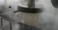 close up of a machine extruding noodles into boiling water.