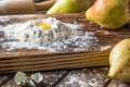 Close up. Broken quail egg in a hill of white flour, surrounded by ripe large pears. Rustic still life. Brown wooden background Royalty Free Stock Photo