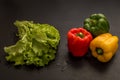 Close up, macro. Flat lay. Three multicolored peppers paprika and a big bunch of fresh green lettuce on black background