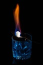 Close up, macro. A glass of absinthe, on it lies a fork with a cube of sugar. Sugar is engulfed in flames of burning fire.