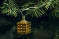 Close up, macro. A golden cube of a festive Christmas garland hanging from a branch. A fragment of a Christmas tree